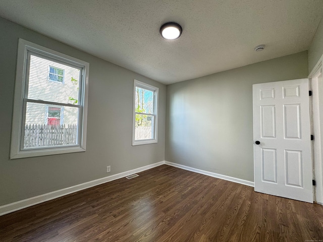 unfurnished room with baseboards, dark wood-style flooring, a textured ceiling, and visible vents