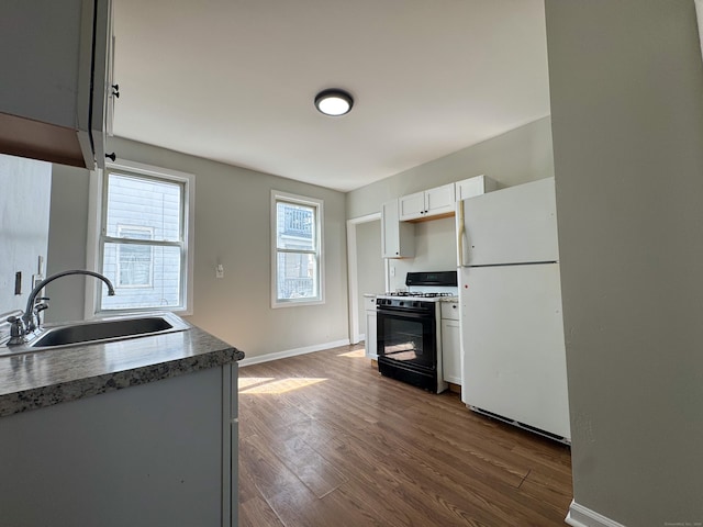 kitchen with freestanding refrigerator, dark wood-style flooring, a sink, and range with gas cooktop