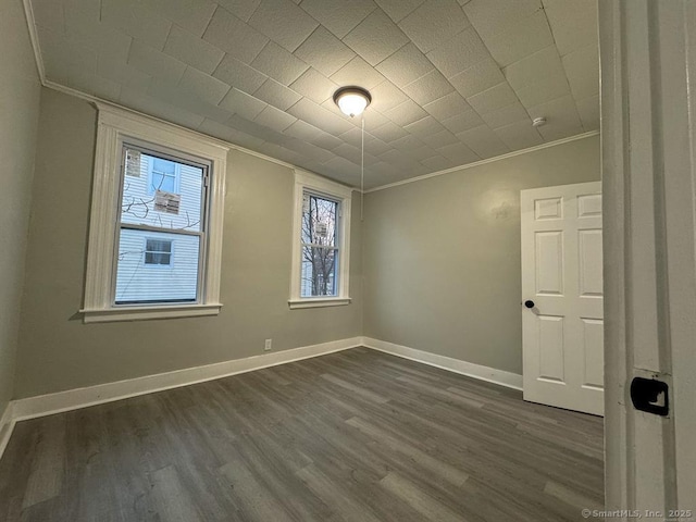 empty room featuring crown molding, baseboards, and dark wood-style floors