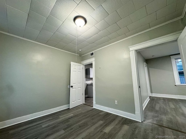 unfurnished bedroom with crown molding, dark wood-style flooring, baseboards, and visible vents