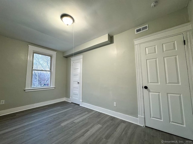 spare room featuring baseboards, visible vents, and dark wood-style floors