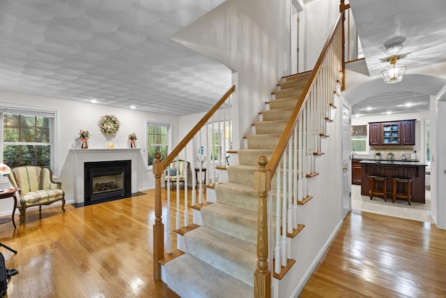 stairs featuring a fireplace with flush hearth, plenty of natural light, wood finished floors, baseboards, and recessed lighting