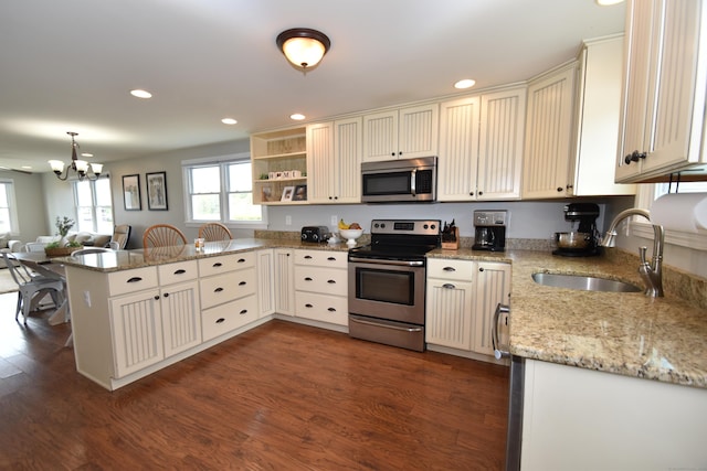 kitchen with dark wood-style flooring, a notable chandelier, appliances with stainless steel finishes, a sink, and a peninsula