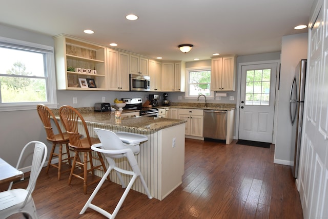 kitchen with dark wood-style flooring, stainless steel appliances, recessed lighting, a peninsula, and a kitchen bar