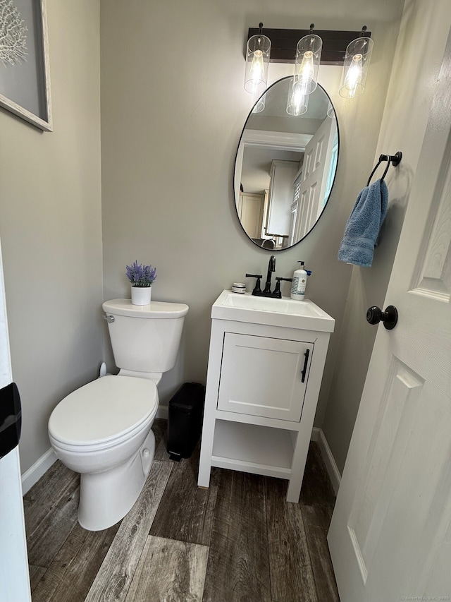 half bath featuring vanity, baseboards, wood finished floors, and toilet