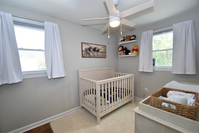 bedroom featuring a crib, baseboards, and ceiling fan