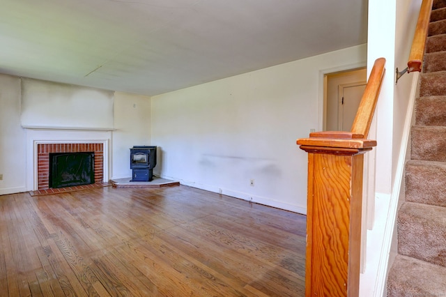 unfurnished living room featuring a wood stove, stairway, wood finished floors, and baseboards