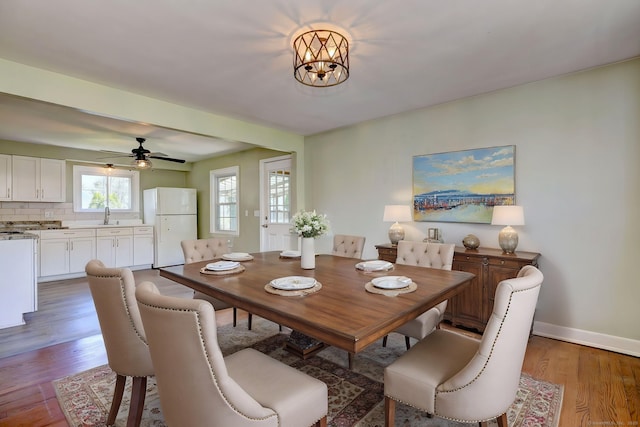 dining space with baseboards, ceiling fan with notable chandelier, and wood finished floors