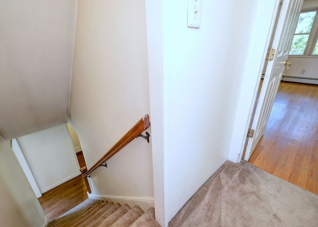 staircase with a baseboard heating unit and wood finished floors