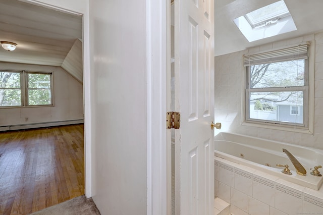 full bath featuring a tub with jets, a skylight, wood finished floors, and a baseboard radiator