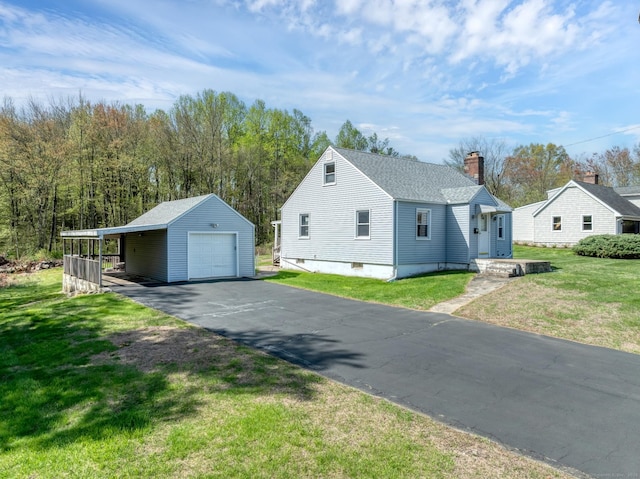 view of side of home with a yard, a chimney, an outbuilding, driveway, and a detached garage
