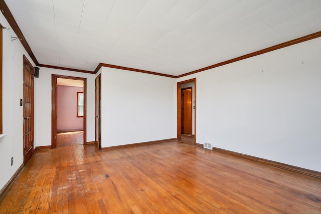 empty room featuring crown molding, baseboards, wood-type flooring, and visible vents