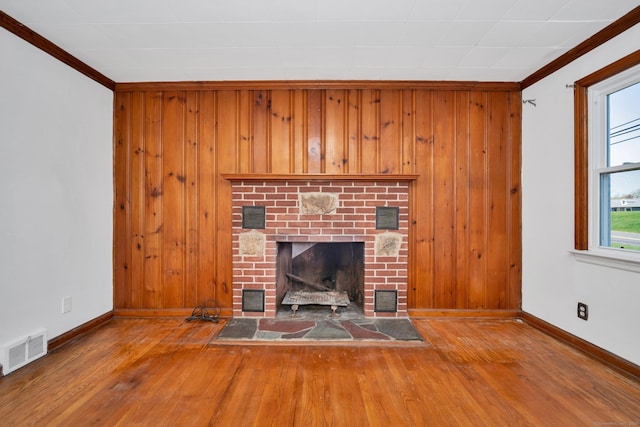 unfurnished living room with baseboards, wood-type flooring, a brick fireplace, and visible vents