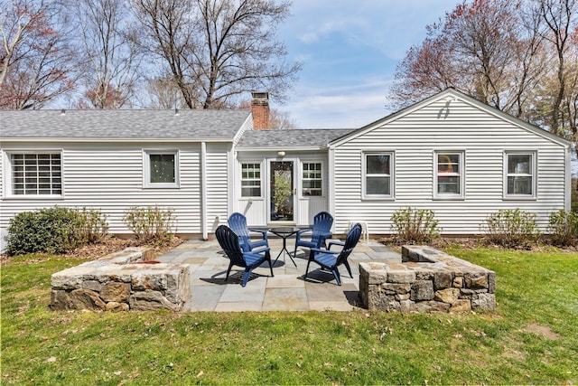 rear view of property with a lawn, a shingled roof, a chimney, and a patio area
