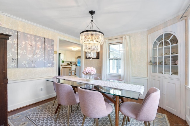 dining room featuring crown molding, wallpapered walls, an inviting chandelier, and wood finished floors
