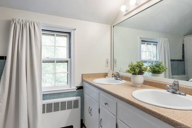 bathroom featuring radiator heating unit, double vanity, a sink, and lofted ceiling