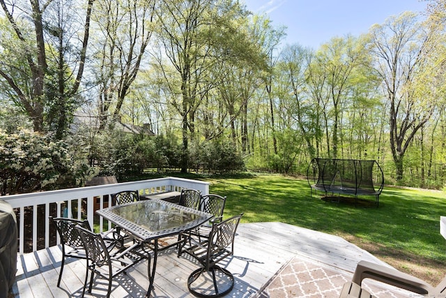 wooden terrace featuring a lawn, outdoor dining area, and a trampoline