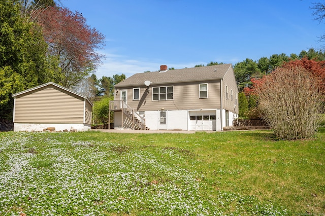 rear view of house featuring a lawn, stairs, an attached garage, and a chimney