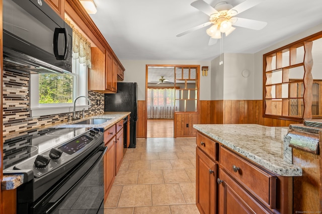 kitchen featuring ceiling fan, a sink, brown cabinetry, a wainscoted wall, and black appliances