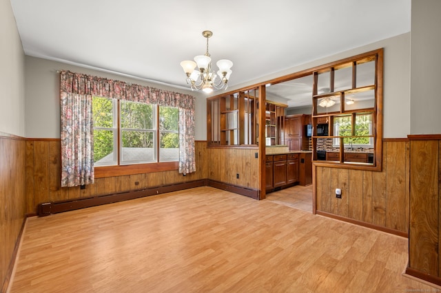 unfurnished dining area featuring wooden walls, a chandelier, and wainscoting
