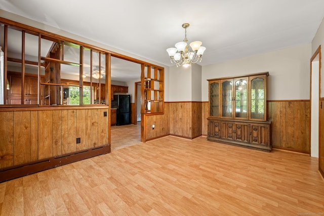 unfurnished dining area featuring an inviting chandelier, wood walls, wainscoting, and light wood-style flooring
