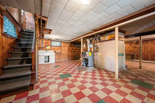 unfinished basement featuring stairway, tile patterned floors, wood walls, and a heating unit