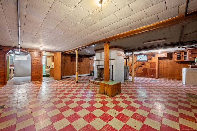 basement featuring a brick fireplace, arched walkways, tile patterned floors, wood walls, and stairs