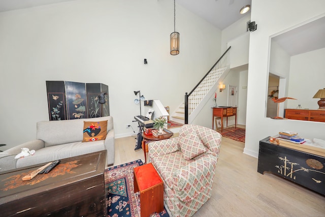 living area with baseboards, high vaulted ceiling, wood finished floors, and stairway