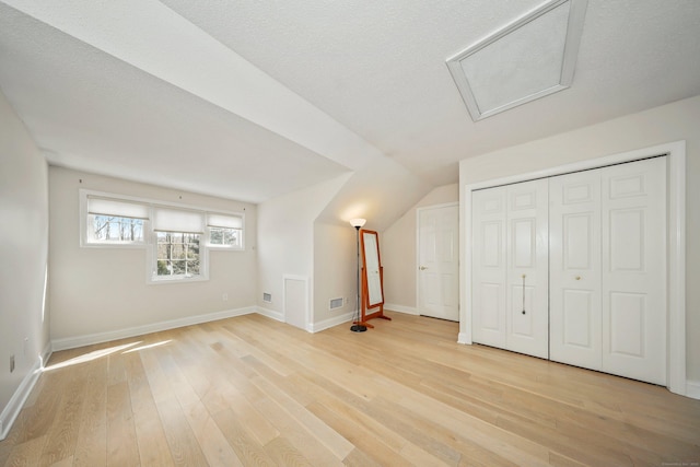 additional living space featuring baseboards, attic access, light wood finished floors, and visible vents