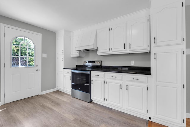 kitchen with dark countertops, stainless steel range with electric cooktop, light wood finished floors, custom range hood, and white cabinetry