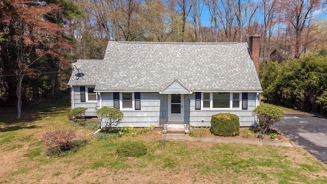 view of front of property featuring a chimney, roof with shingles, and a front lawn