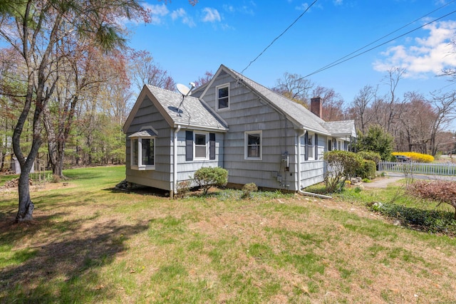 exterior space with a yard, fence, a shingled roof, and a chimney
