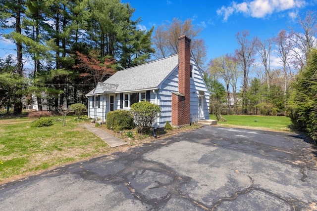 view of front of property featuring roof with shingles, a chimney, and a front yard