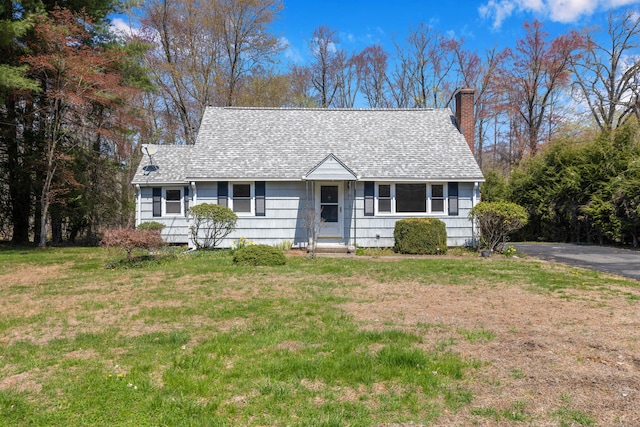 view of front of home with a front lawn, roof with shingles, and a chimney