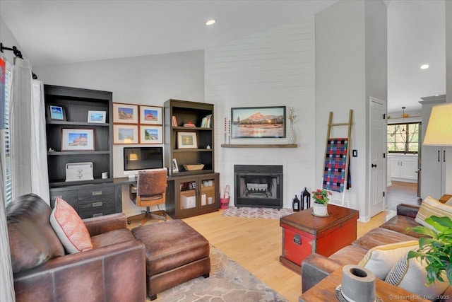 living area featuring recessed lighting, high vaulted ceiling, light wood finished floors, and a fireplace