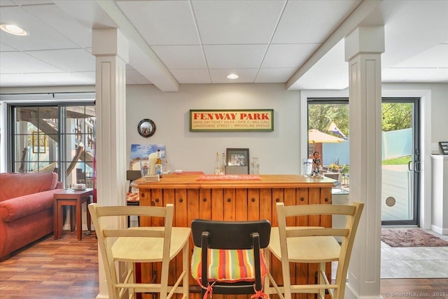 bar featuring a bar, ornate columns, a paneled ceiling, and wood finished floors
