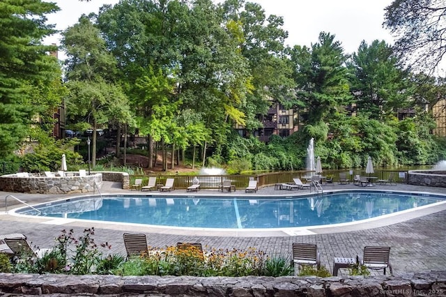community pool with a patio area, fence, and view of wooded area