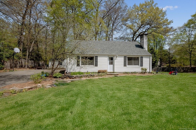 view of front of home featuring fence, a chimney, roof with shingles, and a front yard
