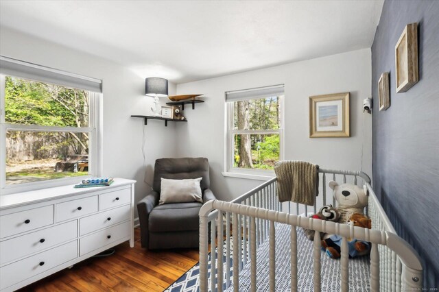 bedroom featuring a nursery area and dark wood finished floors