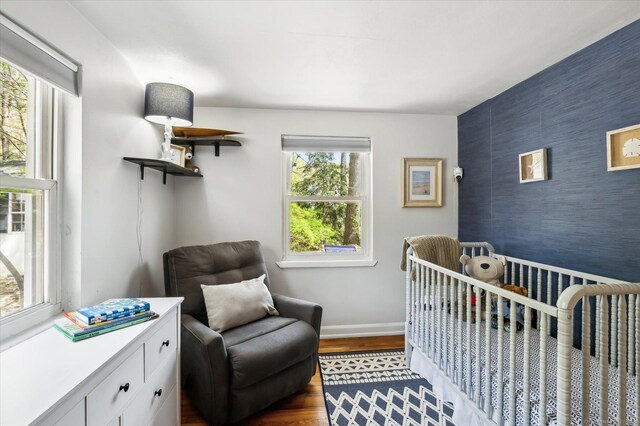 bedroom featuring baseboards, a crib, an accent wall, and dark wood finished floors