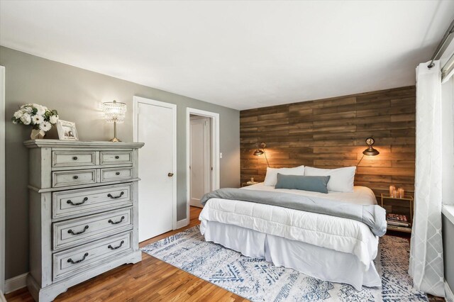 bedroom with wooden walls, baseboards, an accent wall, and wood finished floors