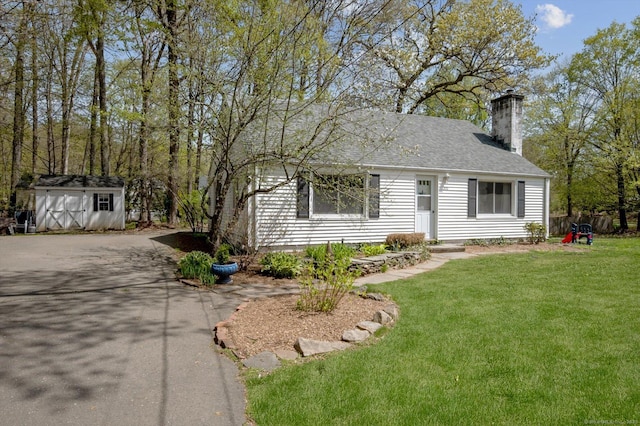 view of front of property featuring a shingled roof, a front lawn, a storage shed, a chimney, and an outdoor structure