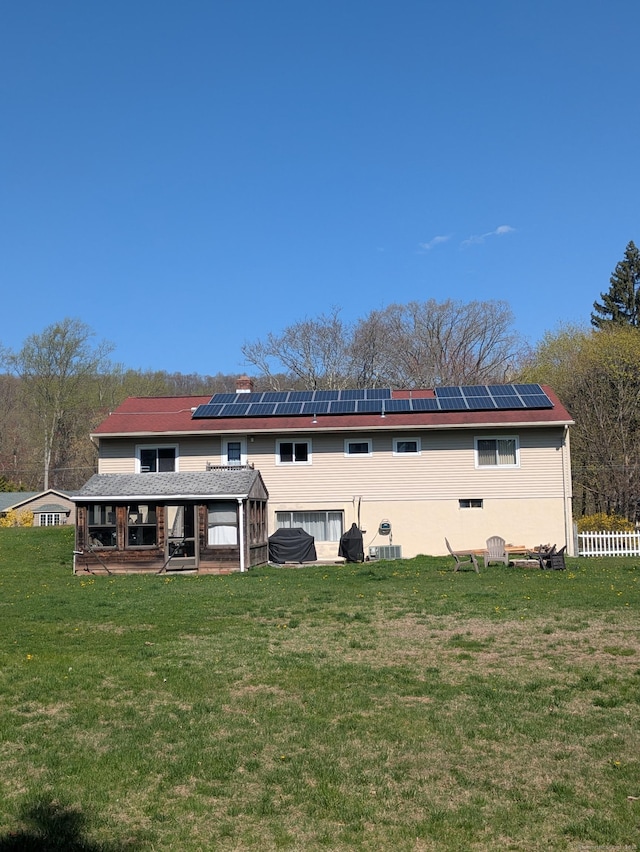 back of house with fence, a yard, and solar panels