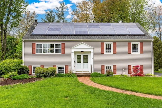 raised ranch with a shingled roof, a front yard, roof mounted solar panels, and a chimney
