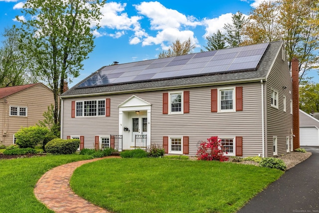split foyer home with a front yard, roof with shingles, solar panels, and a detached garage