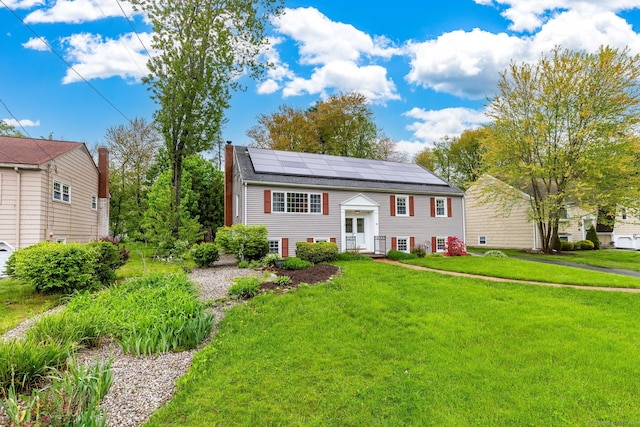 bi-level home with roof mounted solar panels, a front lawn, entry steps, and a chimney