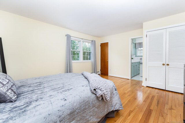 bedroom featuring light wood-type flooring, two closets, ensuite bath, a baseboard heating unit, and baseboards