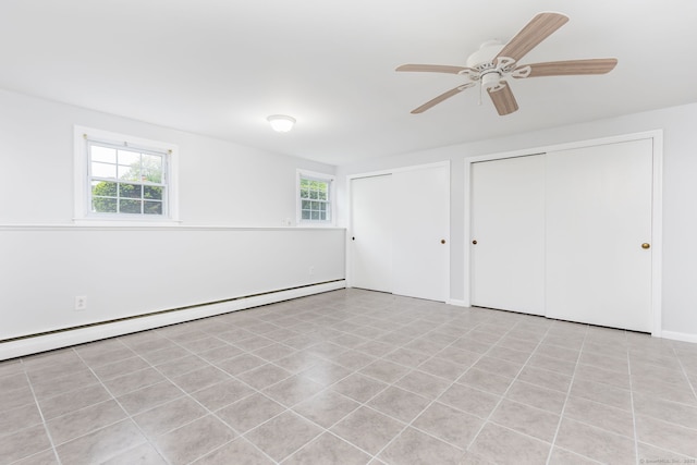 unfurnished bedroom with a baseboard heating unit, two closets, multiple windows, and ceiling fan