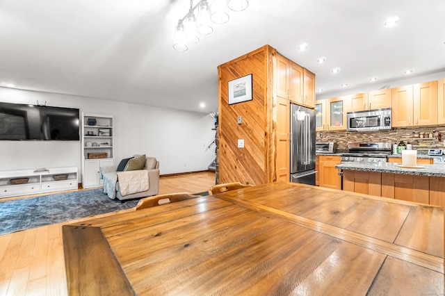 kitchen with appliances with stainless steel finishes, backsplash, open floor plan, glass insert cabinets, and light wood-style floors