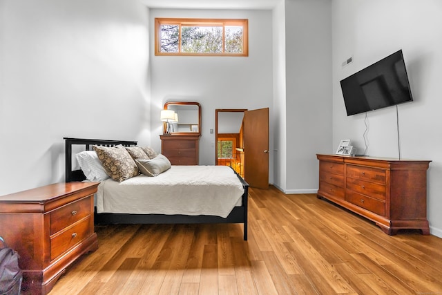 bedroom with a high ceiling, baseboards, and light wood-style floors